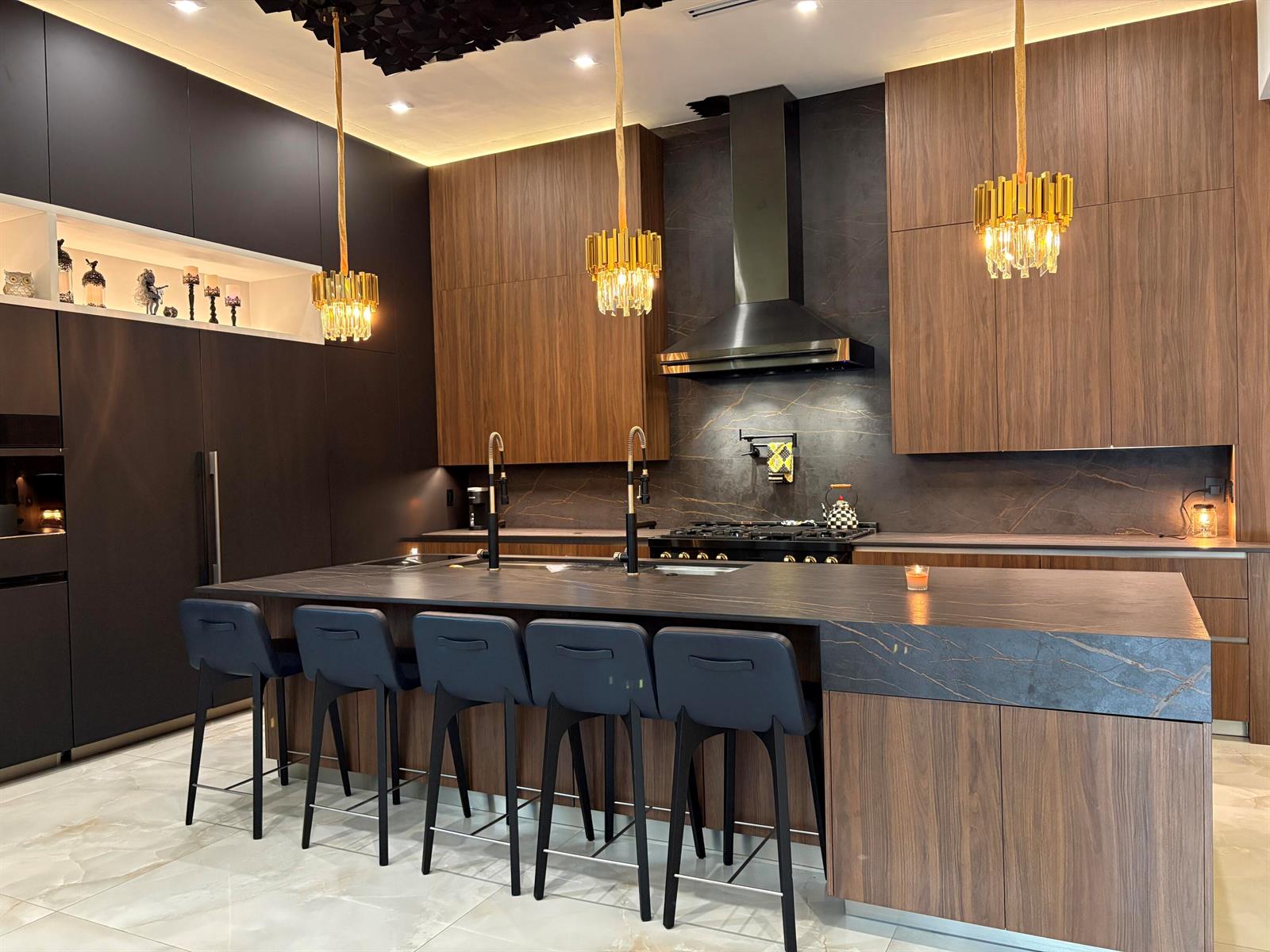 A modern kitchen features dark wood cabinetry, a large stone island, and gold pendant lights — 6935 Long Leaf Drive, Parkland FL 33076, PARKLAND, FL