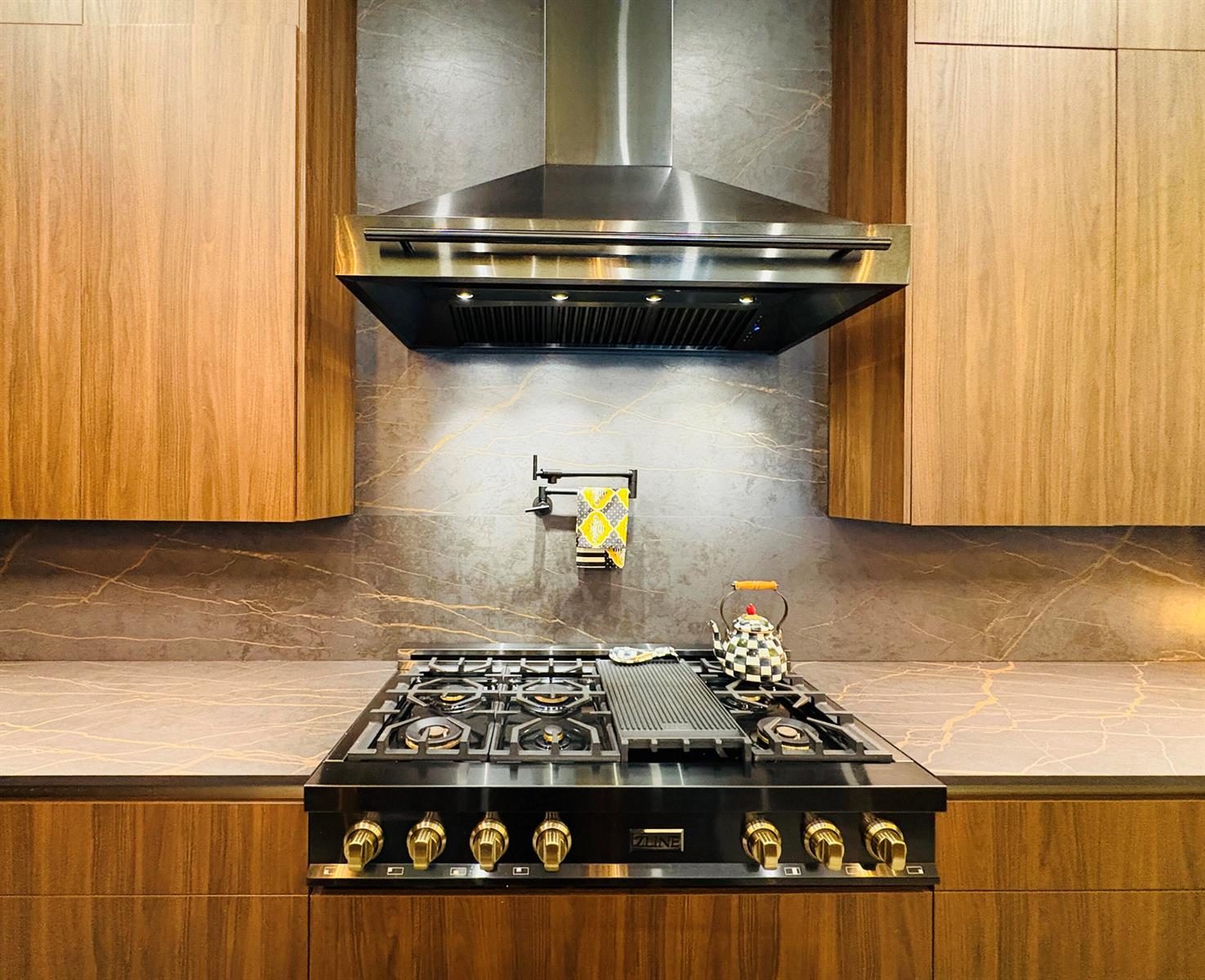 A modern kitchen features wood cabinets, a stone backsplash, and a stainless steel range hood — 6935 Long Leaf Drive, Parkland FL 33076, PARKLAND, FL