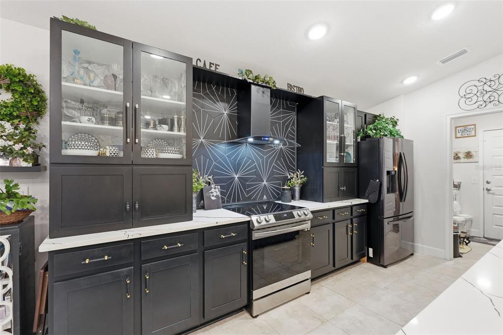 A kitchen features black cabinetry, a geometric patterned backsplash, stainless steel appliances, and white countertops — 11706 SUNDER BERRY STREET, HUDSON, FL