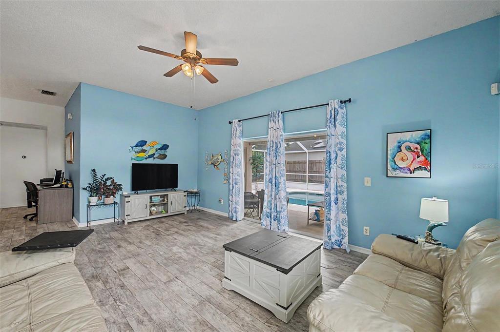 A living room with light blue walls, a ceiling fan, and a view of a pool — 655 SAND RIDGE DRIVE, VALRICO, FL
