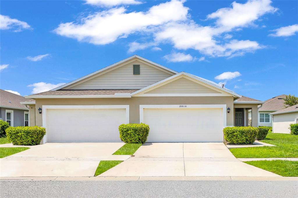 A beige duplex house features two white garage doors and a small front entrance — 20010 ROYAL TERN COURT, LEESBURG, FL