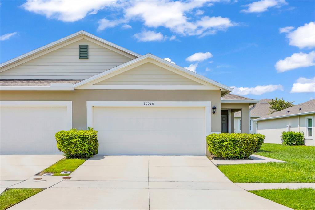 A beige suburban townhouse with a two-car garage and manicured green landscaping under a blue sky — 20010 ROYAL TERN COURT, LEESBURG, FL