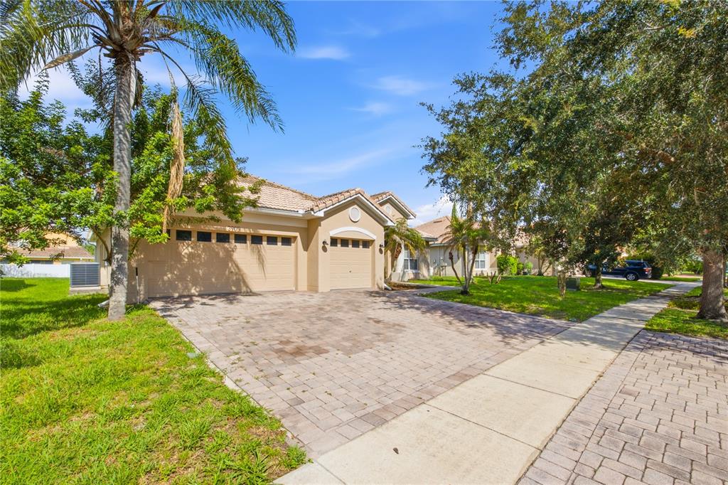 A tan single-story house with a three-car garage and a paved driveway under a blue sky — 3905 BOWFIN TRAIL, KISSIMMEE, FL