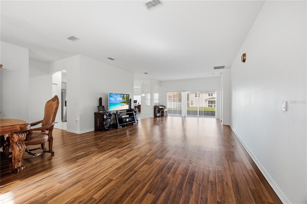 A spacious living room features wood-look flooring, white walls, and a sliding glass door — 3905 BOWFIN TRAIL, KISSIMMEE, FL