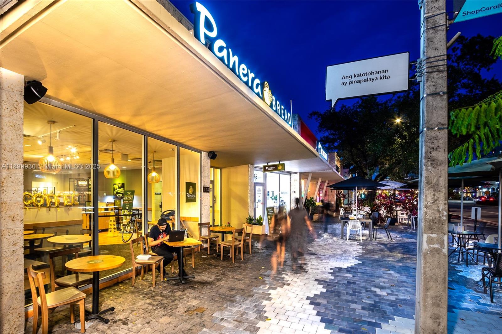 An exterior view of a Panera Bread storefront with outdoor seating at dusk — 137 Miracle Mile, Coral Gables FL 33134, CORAL GABLES, FL
