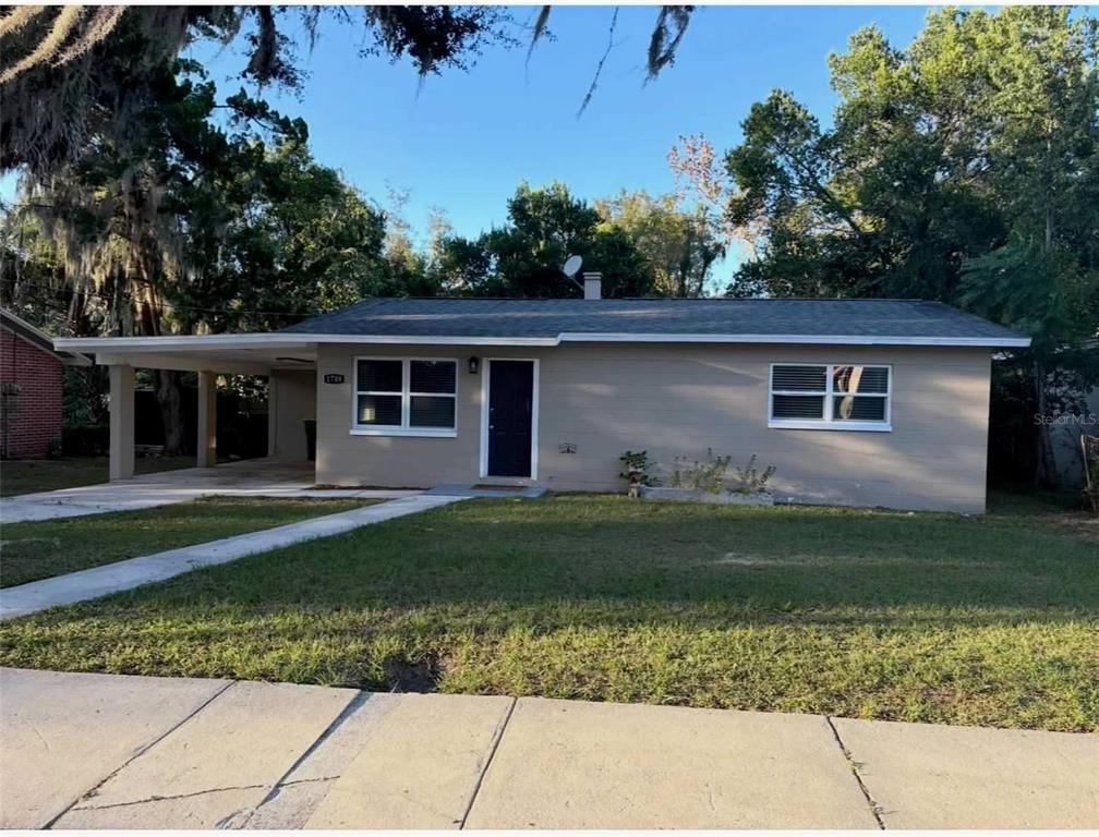 A single-story house with a beige exterior, a dark front door, and an attached carport — 1708 HIGH STREET, LEESBURG, FL