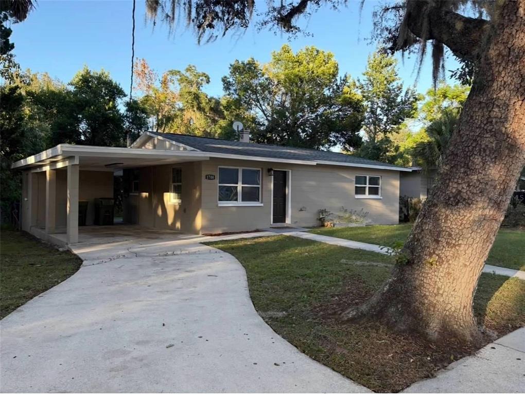 A single-story house with a carport, concrete driveway, and a large tree in the yard — 1708 HIGH STREET, LEESBURG, FL