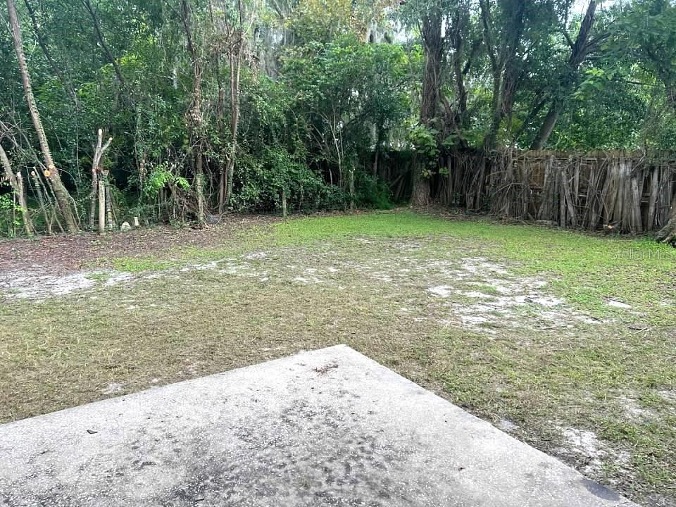 A concrete patio overlooks a grassy backyard bordered by trees and a wooden fence — 1708 HIGH STREET, LEESBURG, FL