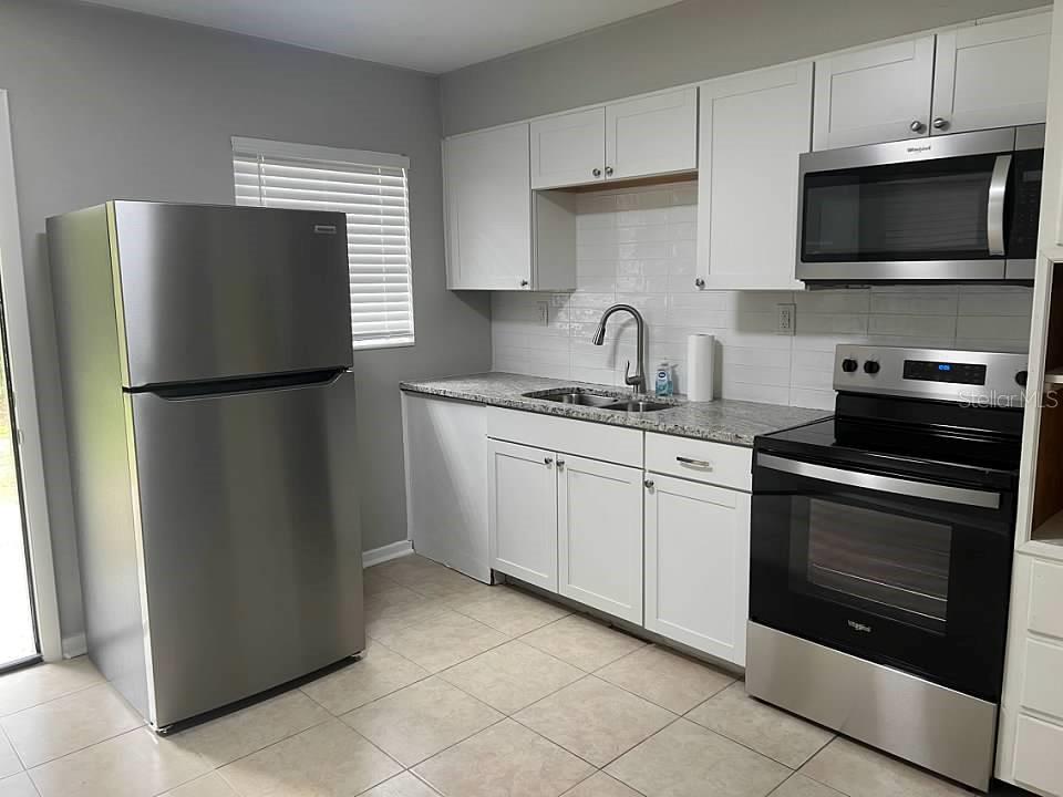 A kitchen with white cabinets, stainless steel appliances, granite countertops, and light tile flooring — 1708 HIGH STREET, LEESBURG, FL