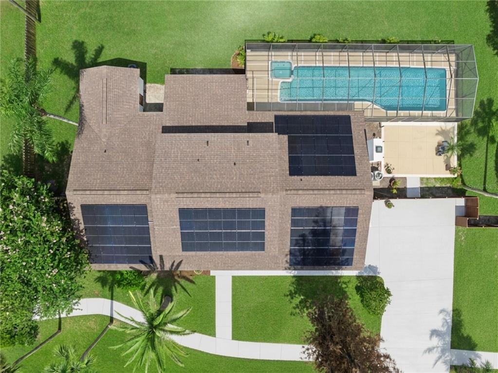 An aerial view shows a house with solar panels on the roof and a screened pool — 537 PELICAN BAY DRIVE, DAYTONA BEACH, FL
