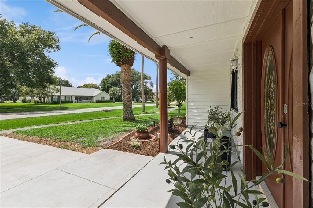 A covered concrete porch features a brown front door and a view of a neighborhood — 537 PELICAN BAY DRIVE, DAYTONA BEACH, FL