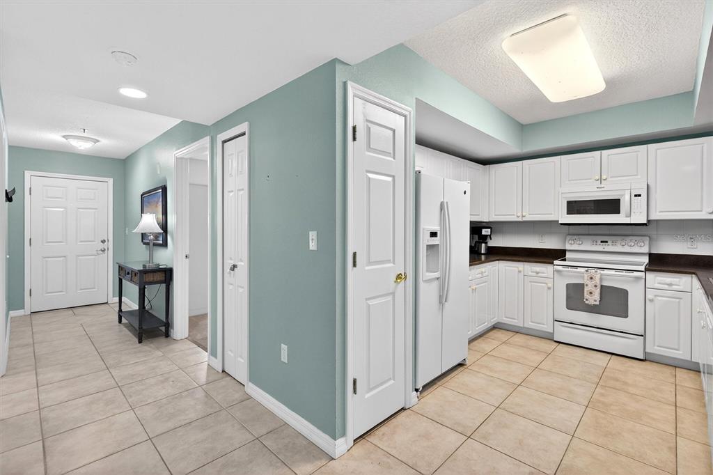 A kitchen with white cabinets and appliances sits adjacent to a tiled entryway and hallway — 5300 S ATLANTIC AVENUE UNIT 9-204, NEW SMYRNA BEACH, FL
