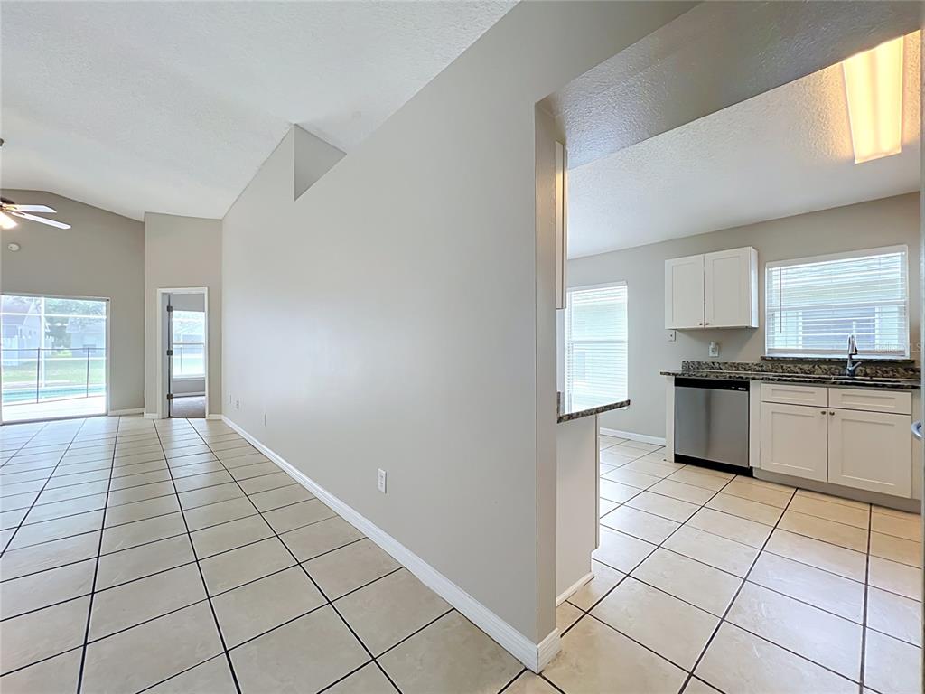 A kitchen with white cabinets and stainless steel appliances opens to a tiled living area — 1005 WINDING WATER WAY, CLERMONT, FL