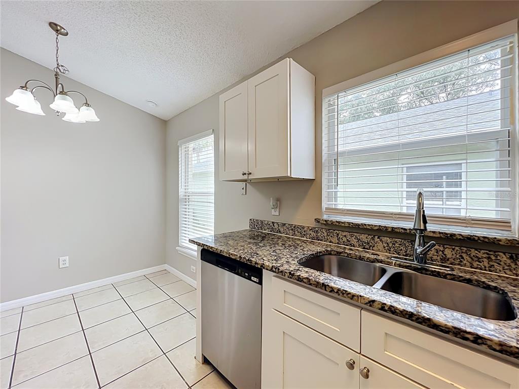 A kitchen features white cabinets, granite countertops, a stainless steel dishwasher, and a double sink — 1005 WINDING WATER WAY, CLERMONT, FL