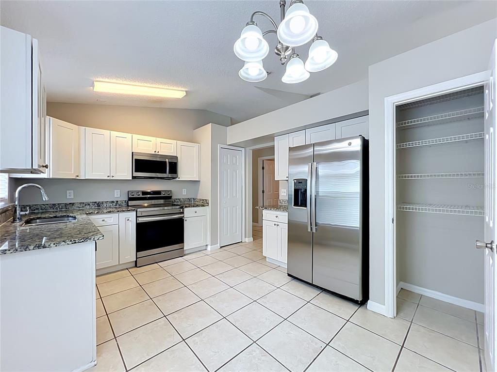 A kitchen features white cabinets, granite countertops, stainless steel appliances, and a tiled floor — 1005 WINDING WATER WAY, CLERMONT, FL