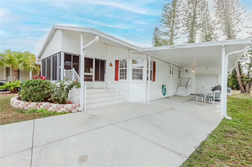A white mobile home features a screened-in porch, a concrete driveway, and a covered carport — 2100 KINGS HIGHWAY UNIT 1006, PORT CHARLOTTE, FL