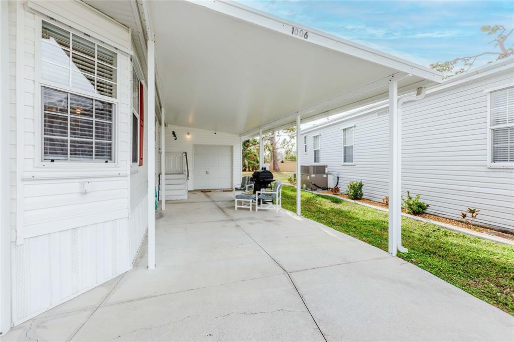 A covered concrete carport sits between two white siding houses with a small grill area — 2100 KINGS HIGHWAY UNIT 1006, PORT CHARLOTTE, FL