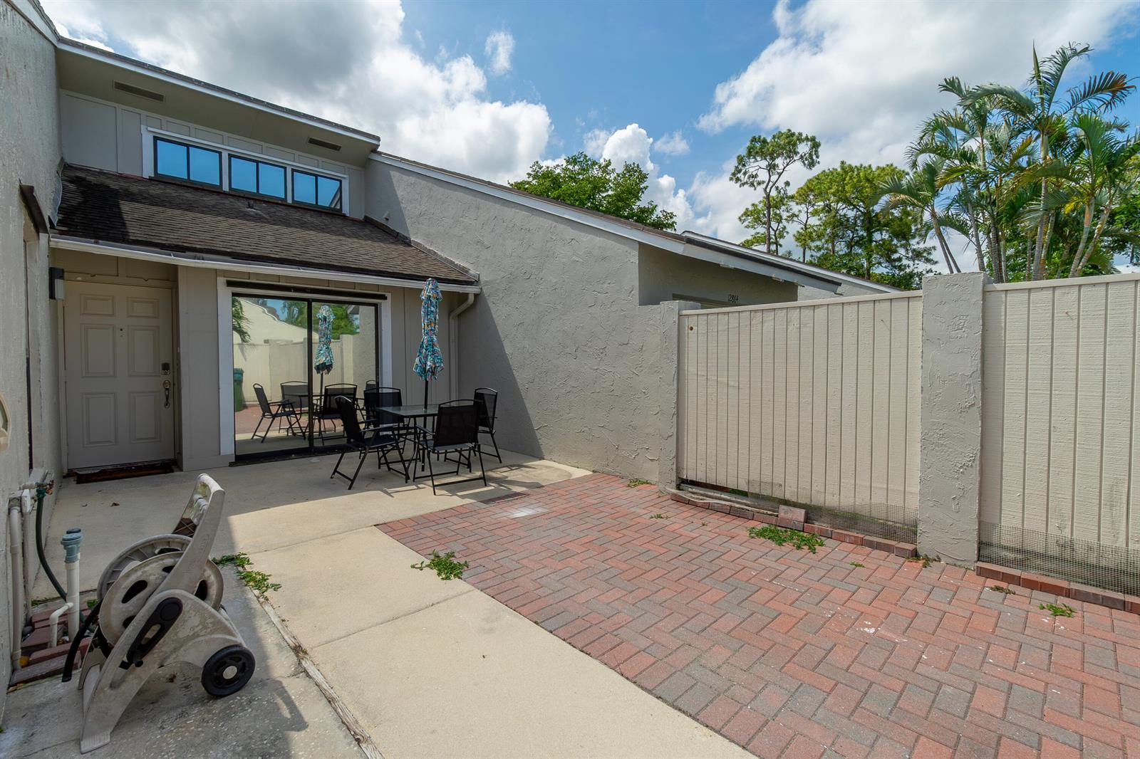 A patio features a brick-paved area, a dining set, and a hose reel near a house — 12858 Spinnaker Lane, Wellington FL 33414, WELLINGTON, FL