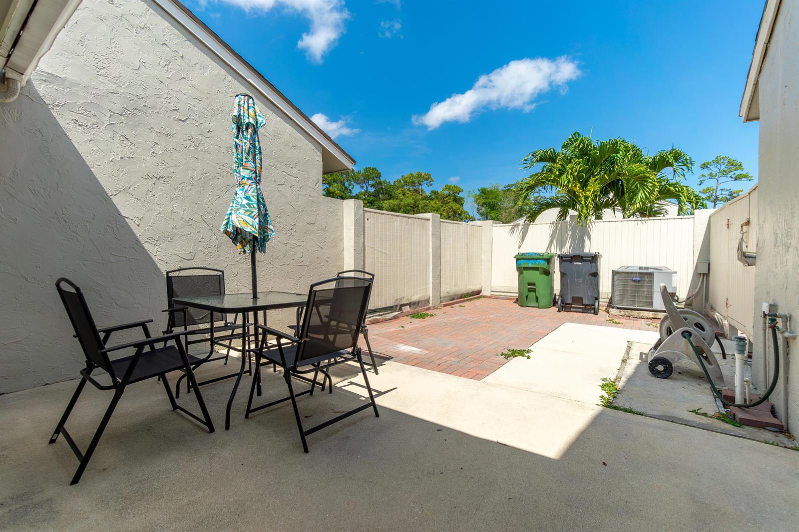 A paved patio features a dining set with an umbrella, two trash bins, and an AC unit — 12858 Spinnaker Lane, Wellington FL 33414, WELLINGTON, FL