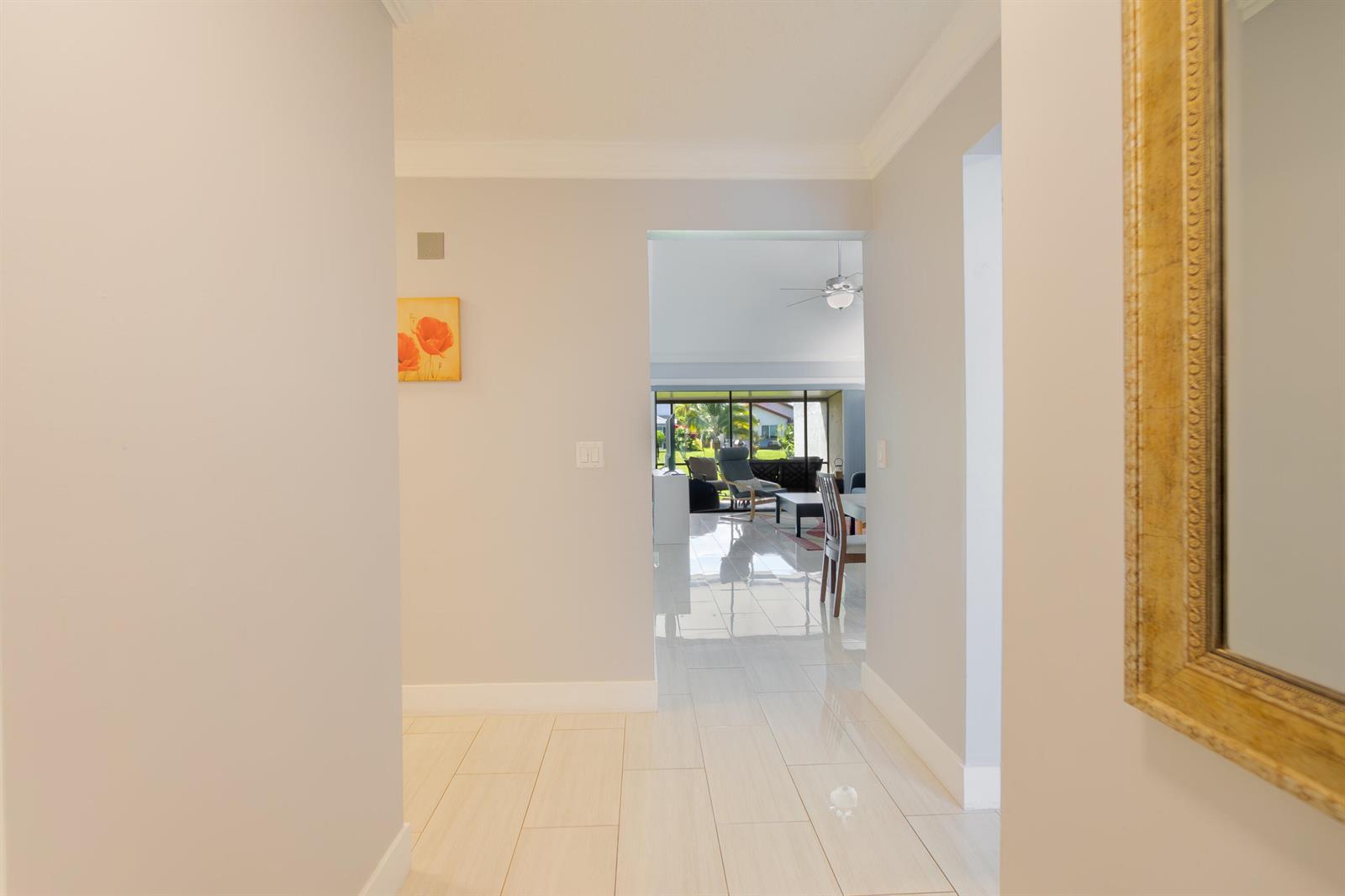 A hallway with light tile floors leads to an open living area with large windows — 12858 Spinnaker Lane, Wellington FL 33414, WELLINGTON, FL