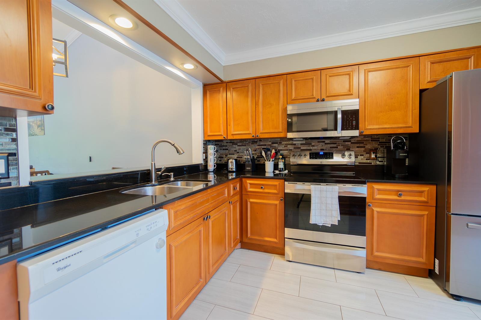 A kitchen features wood cabinets, black countertops, stainless steel appliances, and light-colored tile flooring — 12858 Spinnaker Lane, Wellington FL 33414, WELLINGTON, FL
