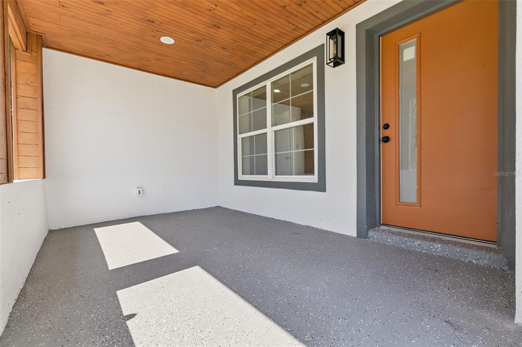 A covered porch features a gray speckled floor, a wood-paneled ceiling, and an orange front door — 10633 WATERTOWN COURT, ORLANDO, FL