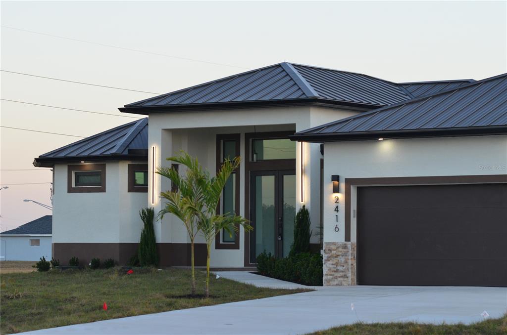 A modern single-story house features a metal roof, white stucco walls, and a brown garage — 2416 DIPLOMAT PARKWAY W, CAPE CORAL, FL