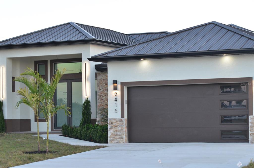 A modern single-story house features a dark metal roof, white stucco walls, and a garage — 2416 DIPLOMAT PARKWAY W, CAPE CORAL, FL