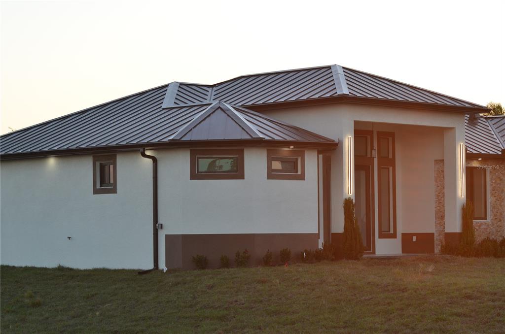 A modern single-story house features a dark metal roof, white stucco walls, and stone accents — 2416 DIPLOMAT PARKWAY W, CAPE CORAL, FL