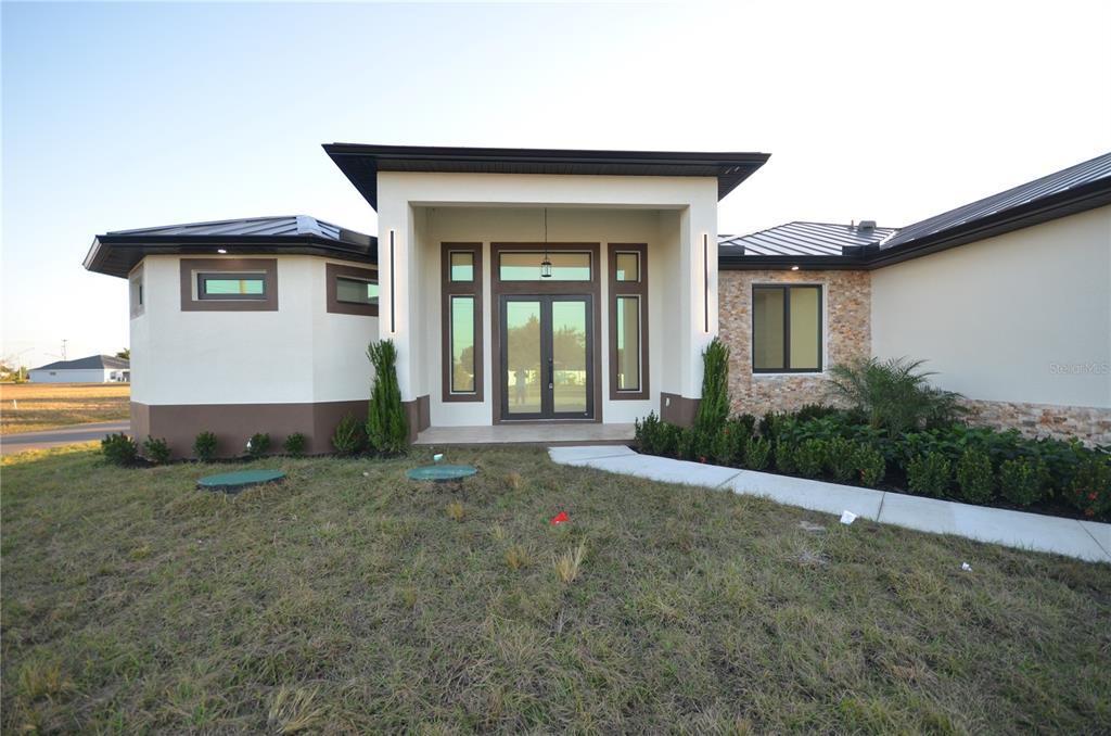 The exterior of a modern house features a covered entryway, stone accents, and metal roofing — 2416 DIPLOMAT PARKWAY W, CAPE CORAL, FL
