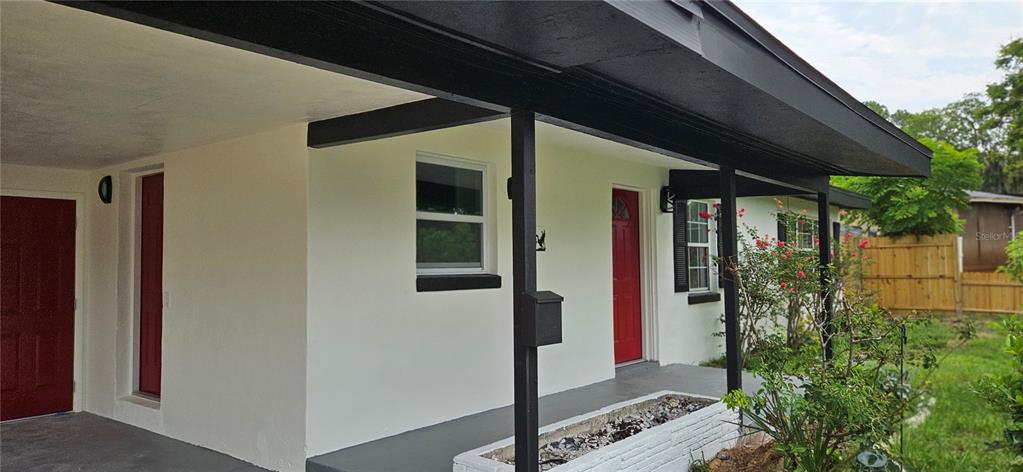 A white house exterior features a covered porch, black trim, and two red doors — 1304 HILLCREST DRIVE, DAYTONA BEACH, FL