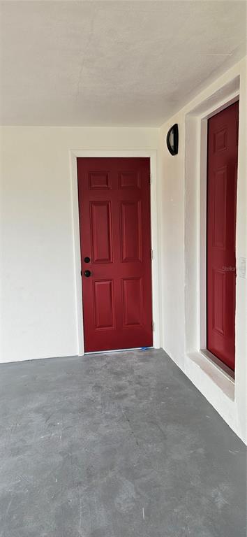 A covered entryway features a gray concrete floor and two red doors with white trim — 1304 HILLCREST DRIVE, DAYTONA BEACH, FL