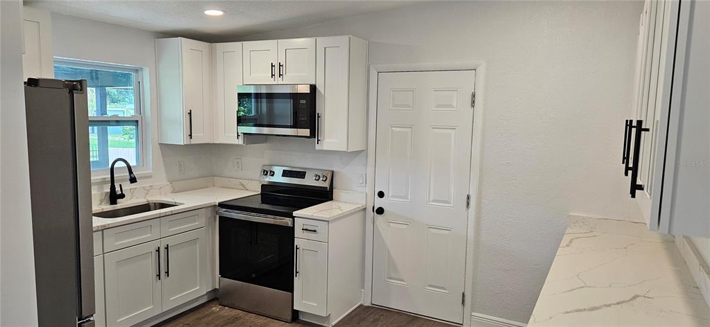 A kitchen features white cabinets, stainless steel appliances, and white countertops with grey veining — 1304 HILLCREST DRIVE, DAYTONA BEACH, FL