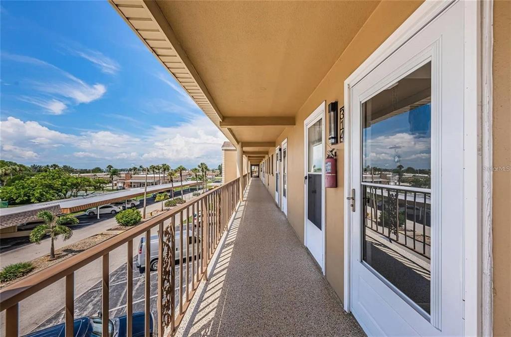 An outdoor apartment walkway features a metal railing, textured flooring, and several white entry doors — 1 BOCA CIEGA POINT BOULEVARD UNIT 314, ST PETERSBURG, FL