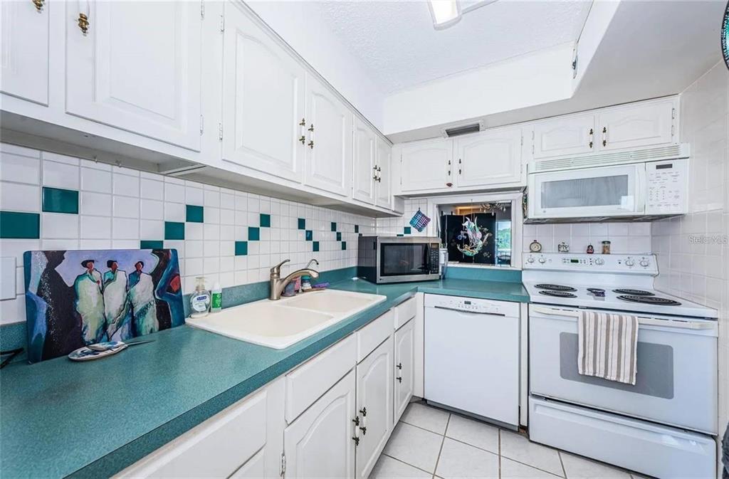 A kitchen with white cabinets, teal countertops, a white tiled backsplash, and white appliances — 1 BOCA CIEGA POINT BOULEVARD UNIT 314, ST PETERSBURG, FL