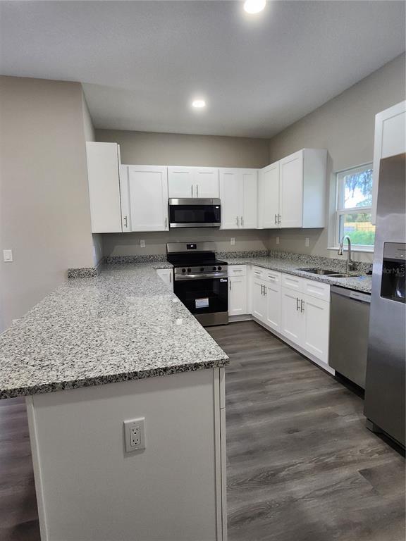 A kitchen features white cabinets, granite countertops, stainless steel appliances, and gray wood-look flooring — 5024 FINDERS COURT, TAMPA, FL