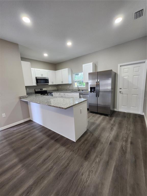 A kitchen with white cabinets, granite countertops, stainless steel appliances, and gray wood-look flooring — 5024 FINDERS COURT, TAMPA, FL