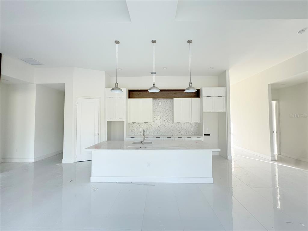 A modern kitchen features white cabinetry, a large central island, and three pendant lights — 23372 ROSEWOOD AVENUE, PUNTA GORDA, FL