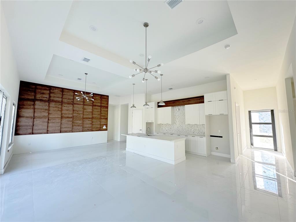 A bright, open-concept kitchen and living area features white cabinetry, a large island, and wood-paneled walls — 23372 ROSEWOOD AVENUE, PUNTA GORDA, FL