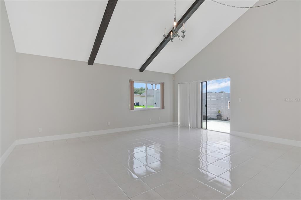 A bright living room features vaulted ceilings with exposed beams, tile flooring, and sliding doors — 2655 BARKSDALE COURT, CLEARWATER, FL