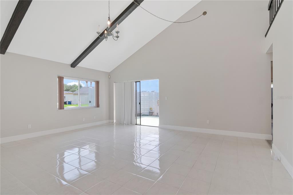 An empty living room features vaulted ceilings with exposed beams, tile flooring, and sliding doors — 2655 BARKSDALE COURT, CLEARWATER, FL