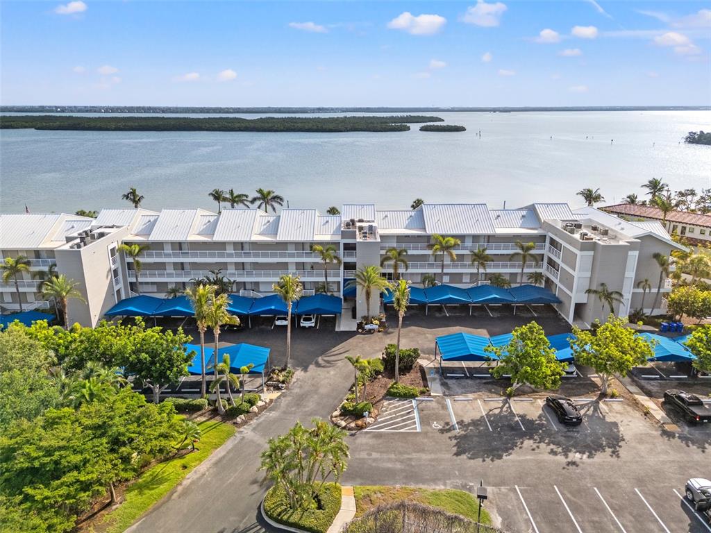 An aerial view shows a multi-story apartment building with covered parking and waterfront views — 615 DREAM ISLAND PLACE UNIT 210, LONGBOAT KEY, FL