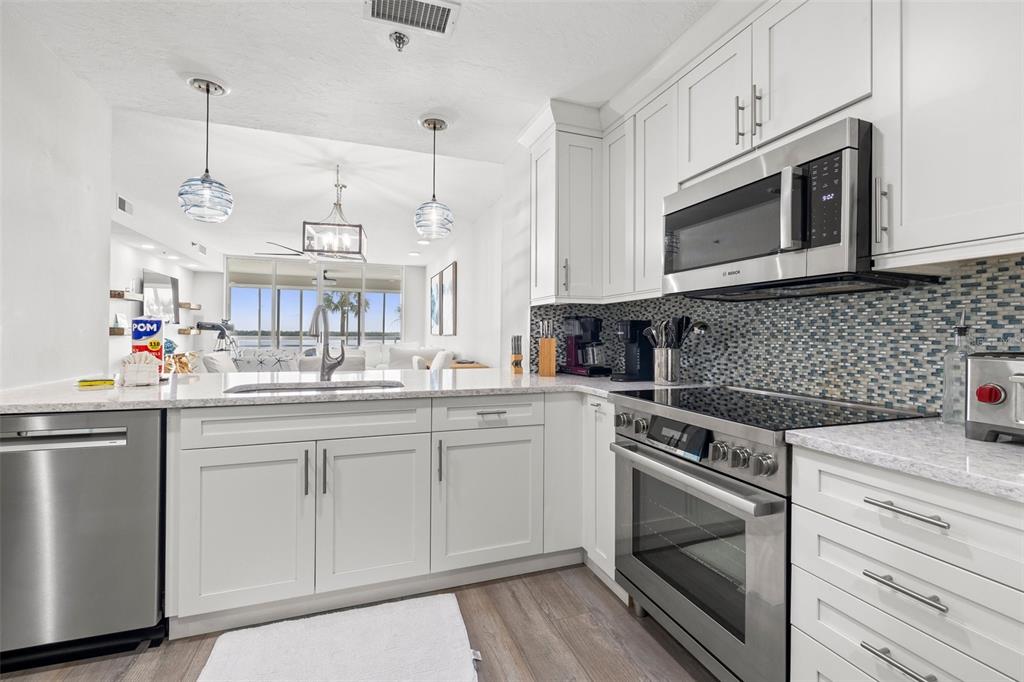 A modern kitchen features white cabinets, stainless steel appliances, and a mosaic tile backsplash — 615 DREAM ISLAND PLACE UNIT 210, LONGBOAT KEY, FL