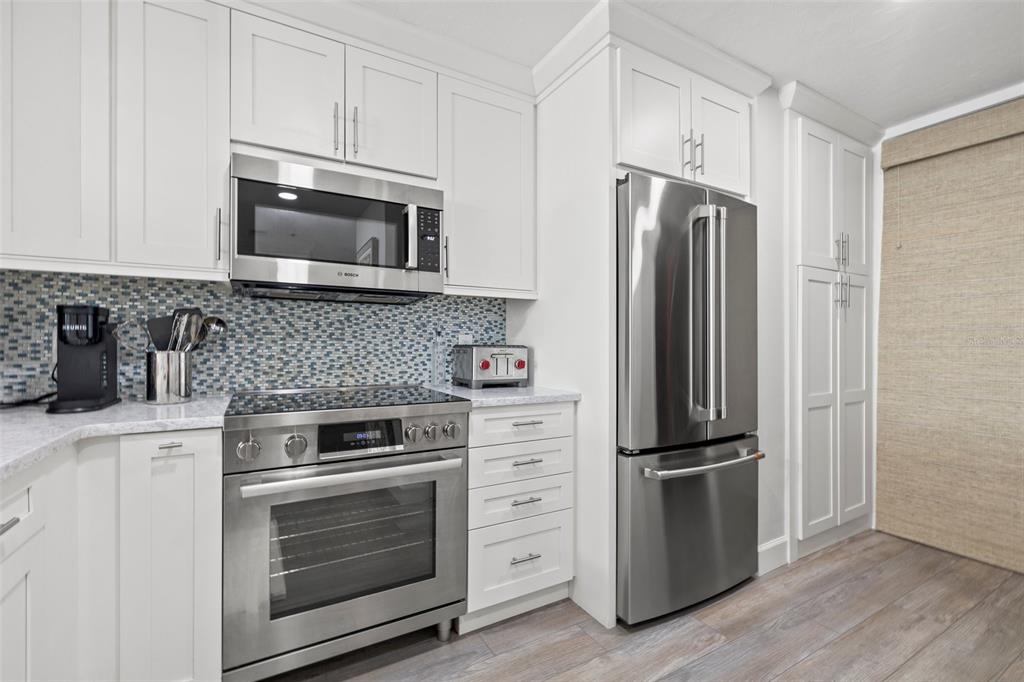 A kitchen features white cabinetry, stainless steel appliances, and a blue mosaic tile backsplash — 615 DREAM ISLAND PLACE UNIT 210, LONGBOAT KEY, FL