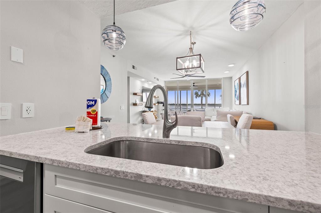 A kitchen sink with a faucet sits on a white countertop overlooking a living area — 615 DREAM ISLAND PLACE UNIT 210, LONGBOAT KEY, FL