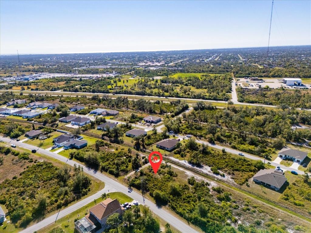 An aerial view shows a vacant, wooded lot marked with a red pin in a neighborhood — 9235 WALDREP STREET, PORT CHARLOTTE, FL