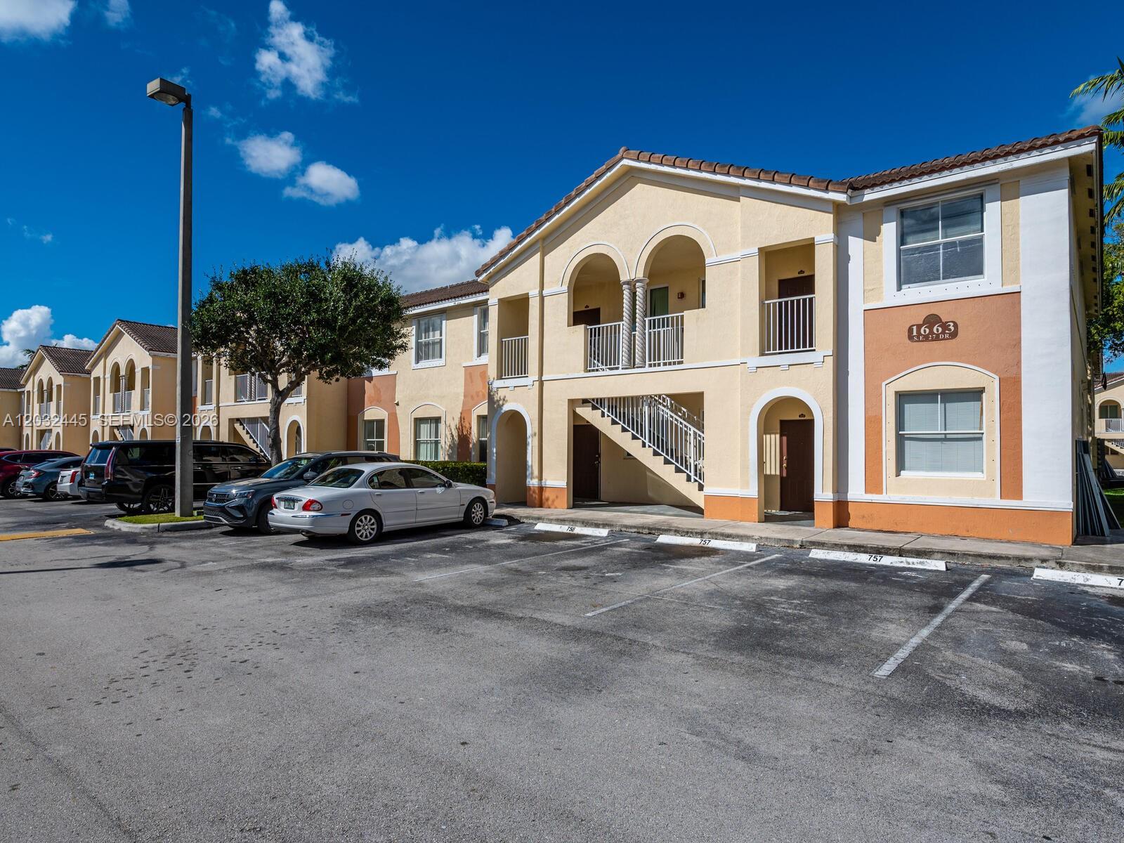 A two-story apartment building with a beige stucco exterior and a parking lot in front — 1663 SE 27th Dr # 108, Homestead FL 33035, HOMESTEAD, FL