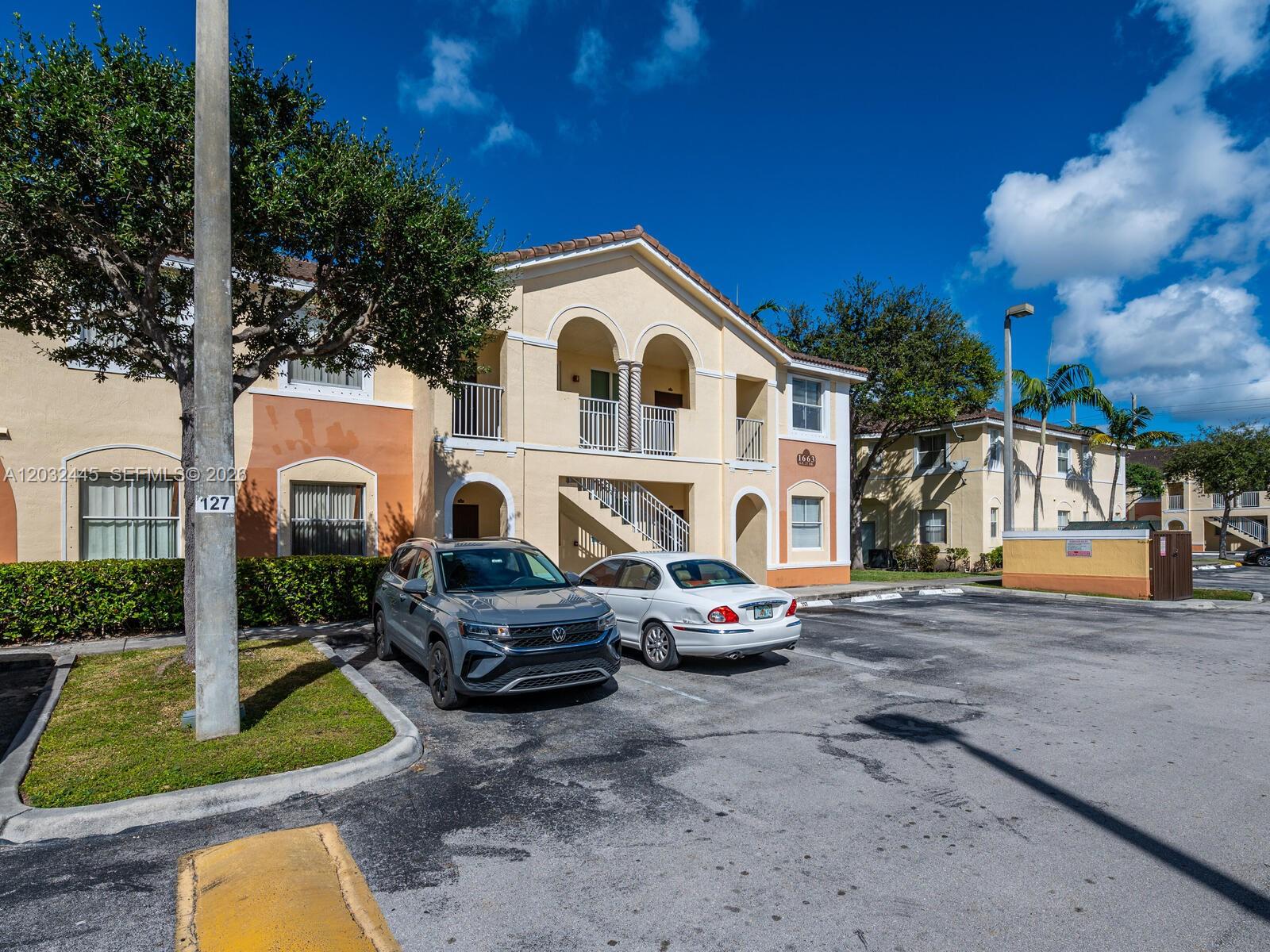 A two-story apartment building with beige stucco walls and two parked cars in front — 1663 SE 27th Dr # 108, Homestead FL 33035, HOMESTEAD, FL