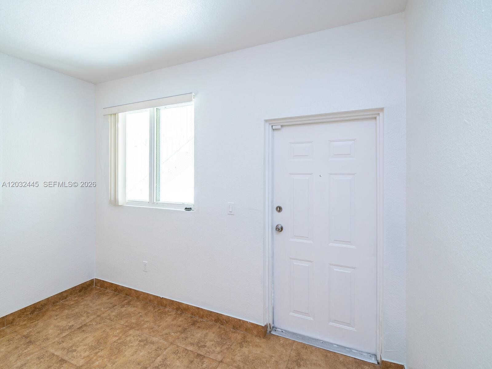 A room with white walls, tile flooring, a window with blinds, and a white door — 1663 SE 27th Dr # 108, Homestead FL 33035, HOMESTEAD, FL