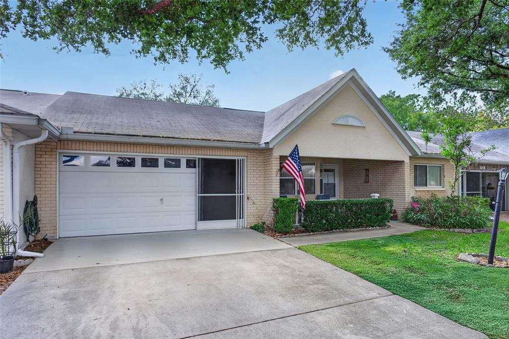 A single-story brick house features a garage, a covered porch, and an American flag — 9060 SW 96TH LANE UNIT B, OCALA, FL